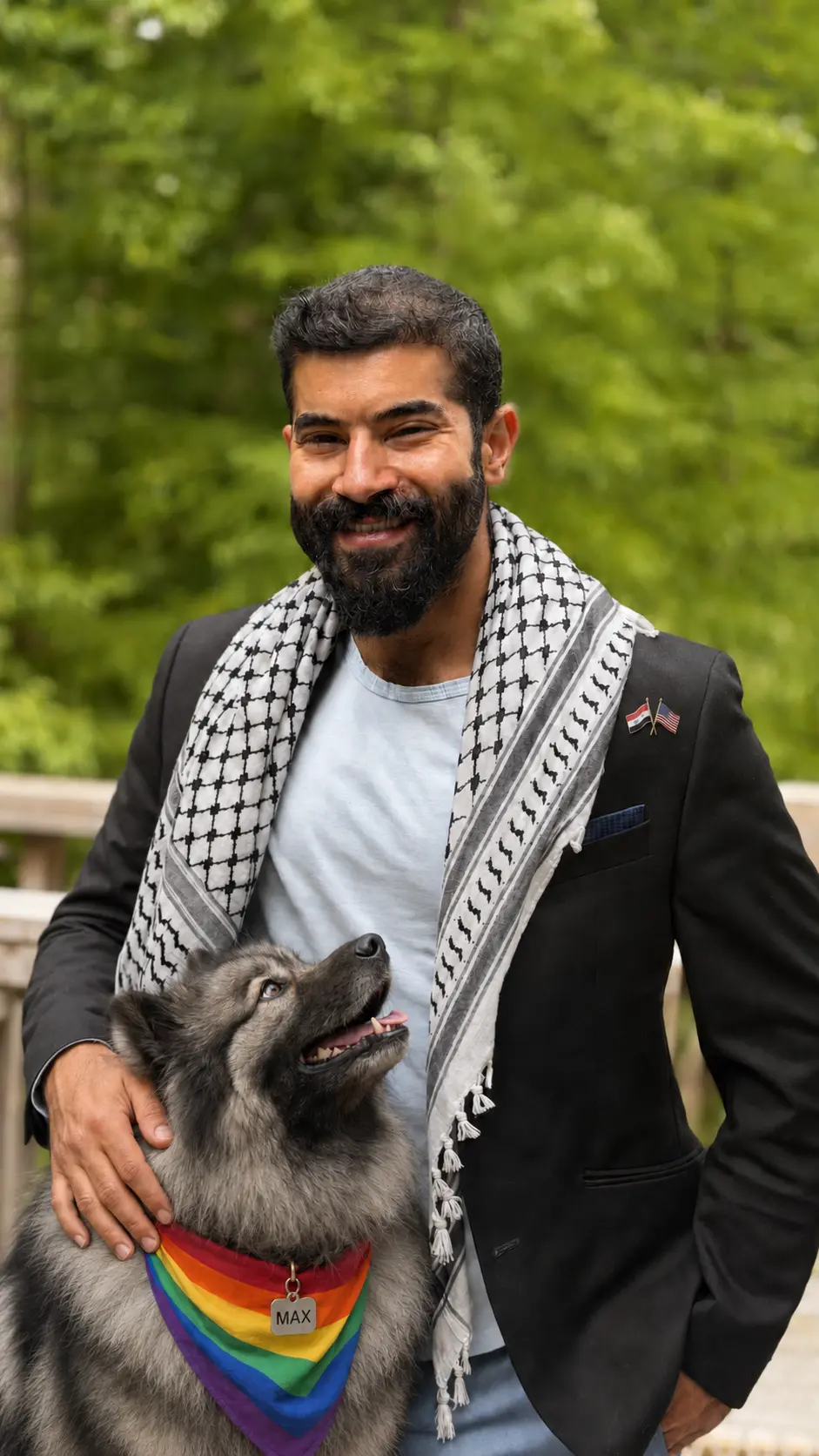 Ali T. Harris, RN, BSN, smiling outdoors in a black blazer and black-and-white keffiyeh as Max, a Keeshond wearing a rainbow Pride bandana, looks up at him